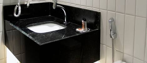 A bathroom with a black sink, white tiles, a toilet, and a hairdryer on the counter.