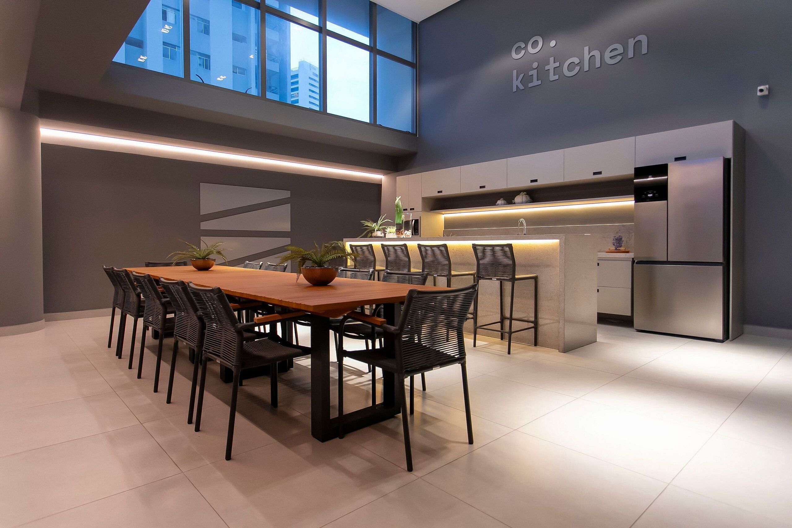 A modern kitchen with a dining area, featuring a large island, built-in appliances, and a view of the city through large windows.