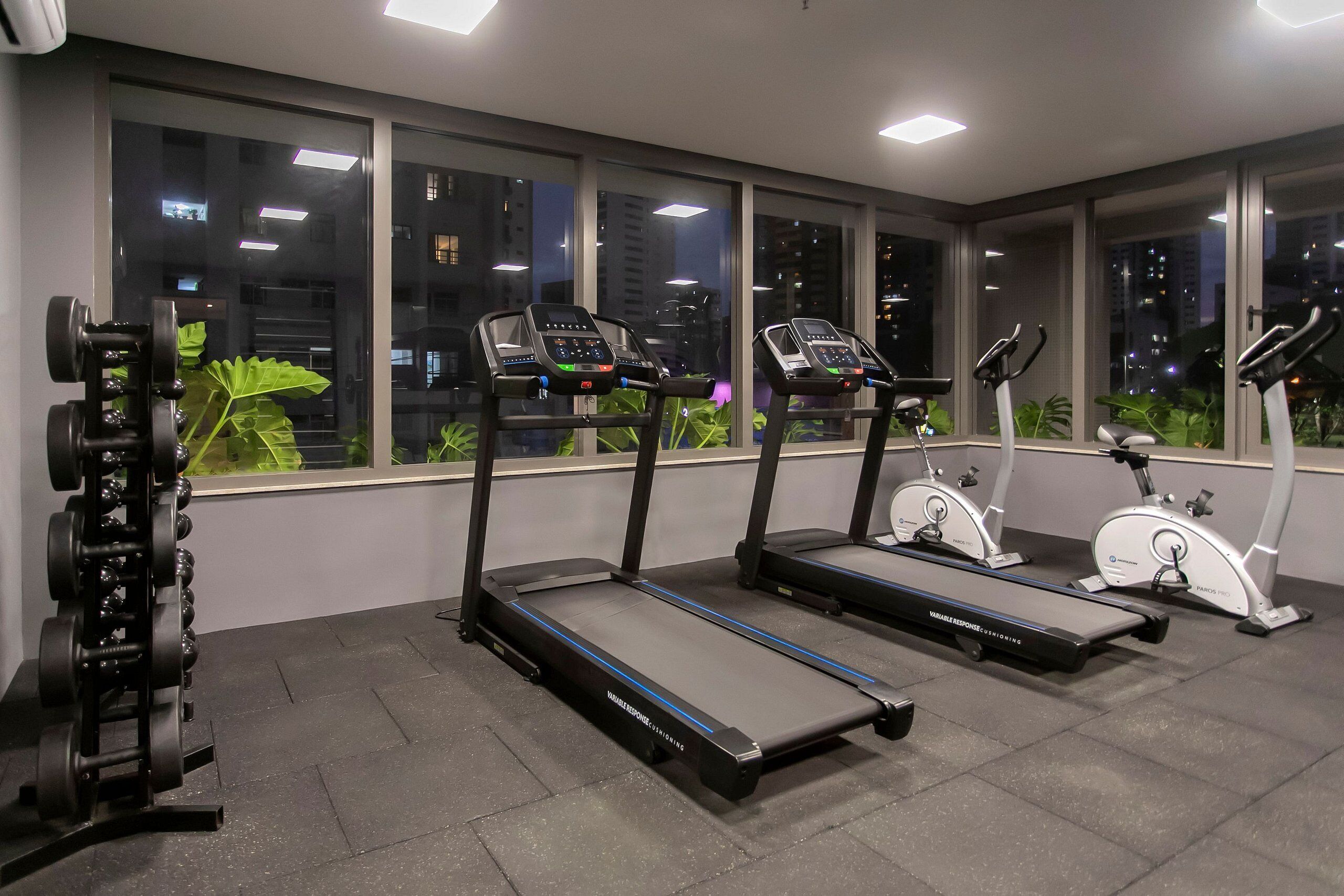 Un gimnasio con cintas de correr, una bicicleta estática y un soporte para pesas.