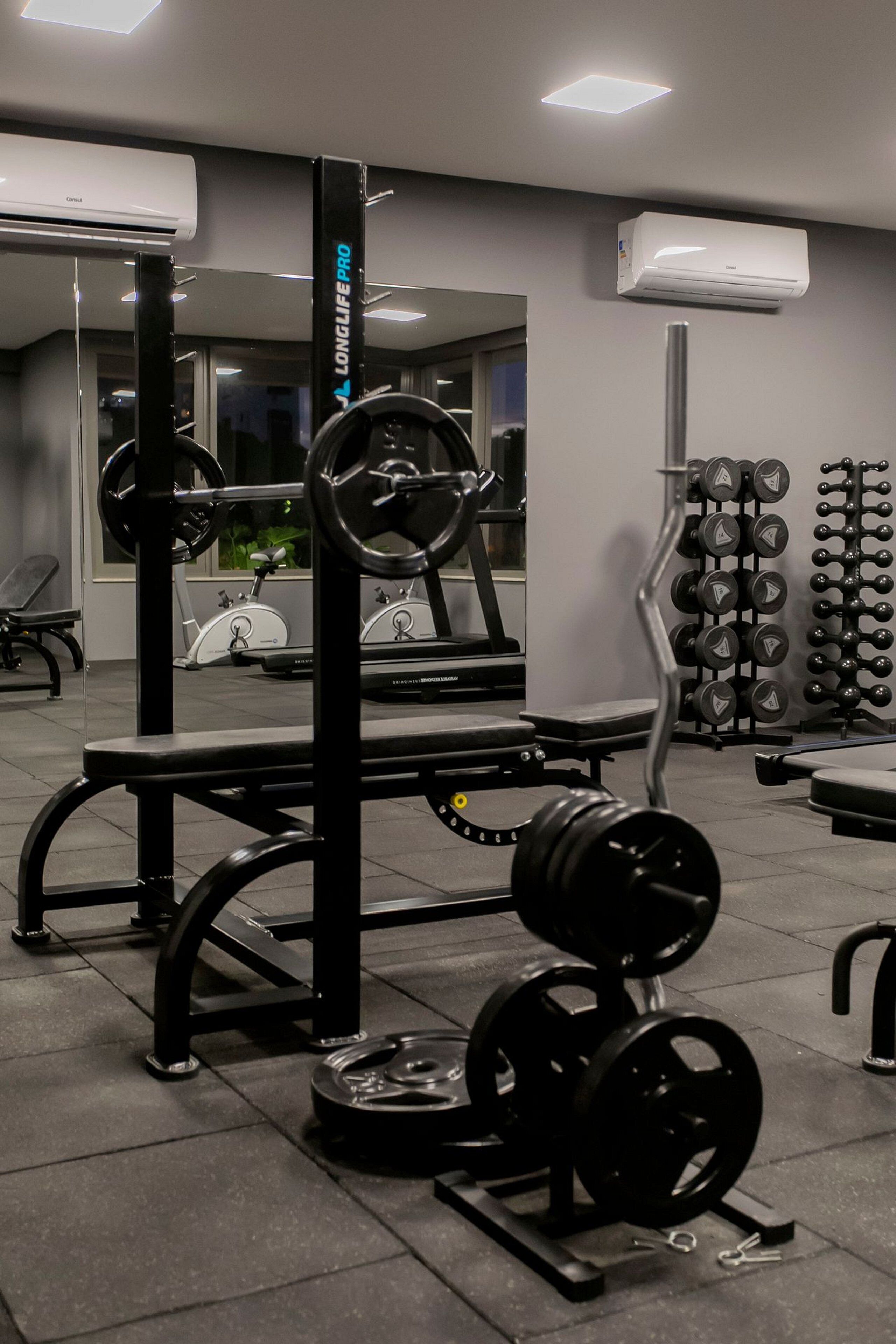 A gym with weightlifting equipment, treadmills, and a wall-mounted air conditioning unit.