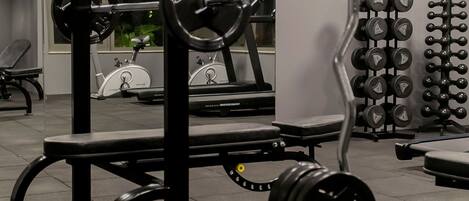 A gym with weightlifting equipment, treadmills, and a wall-mounted air conditioning unit.