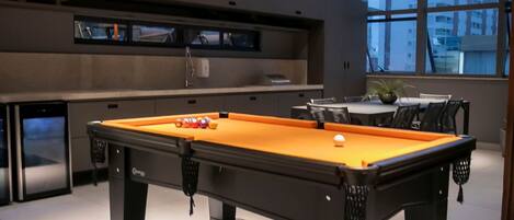 A pool table in a modern room with a large window and a sign reading "espaço grill".