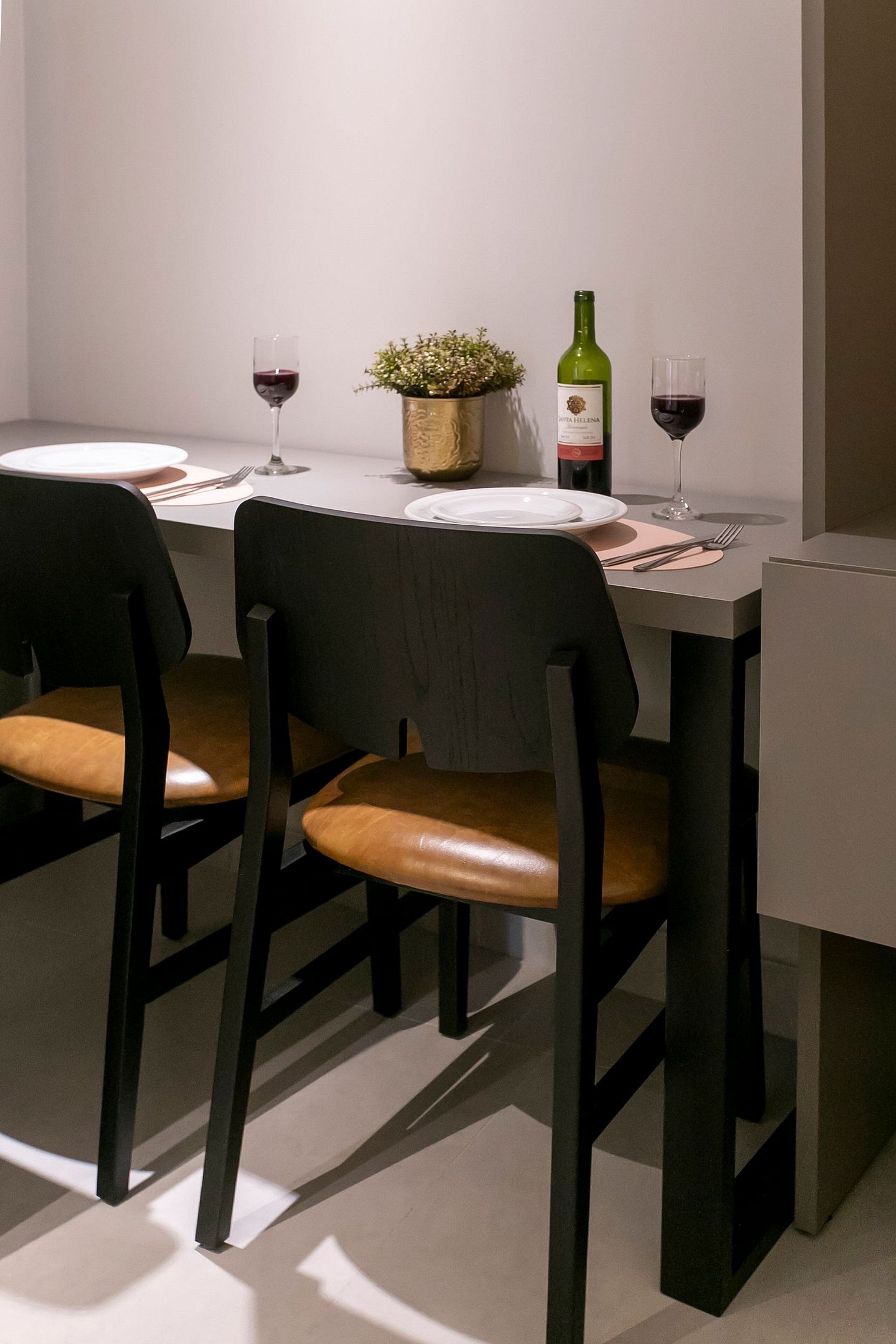 Uma mesa de jantar com duas cadeiras, uma garrafa de vinho e uma pequena planta sobre a mesa.
