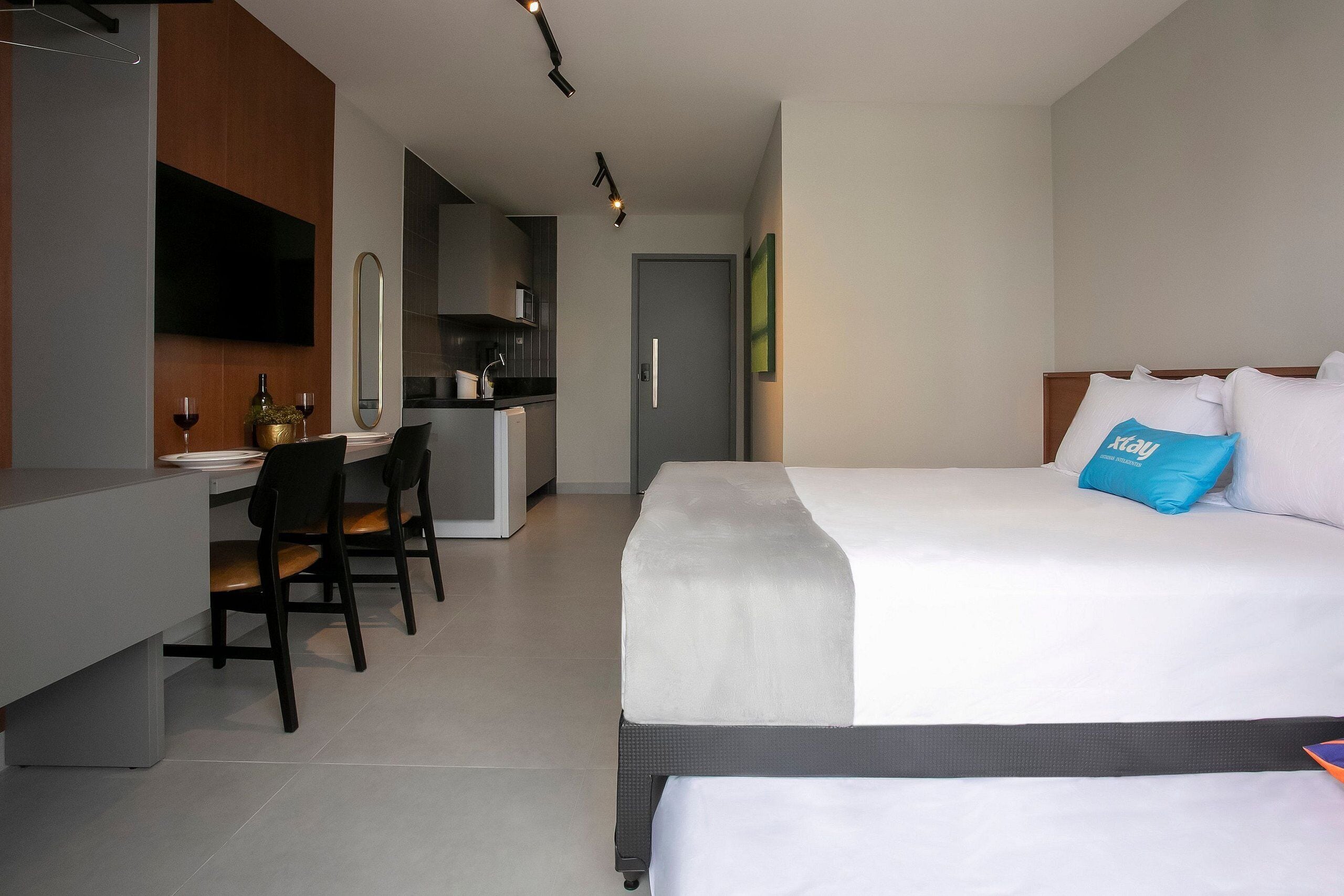 Ein Hotelzimmer mit Bett, Schreibtisch, Stühlen, Fernseher und einer Küchenzeile.