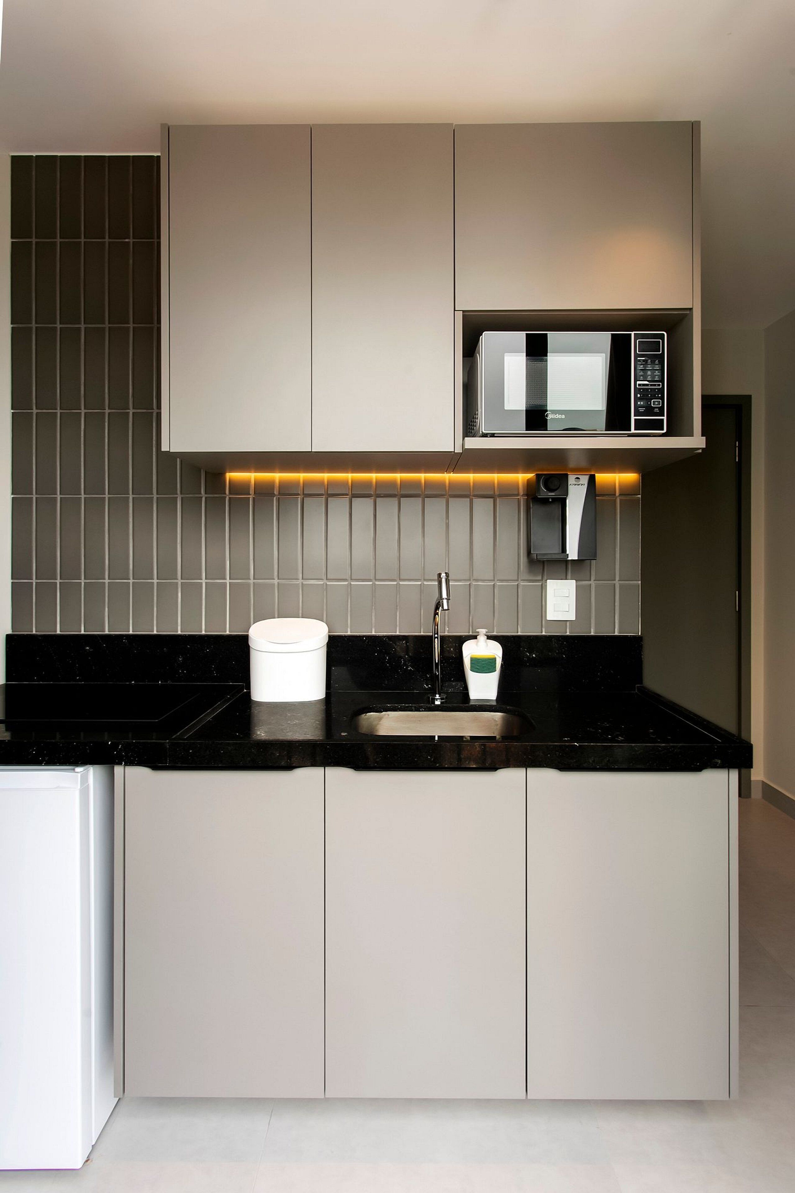 Una cocina moderna con encimera negra, microondas integrado y un lavabo.
