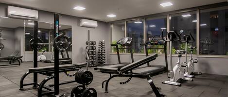 Un gimnasio con equipo de levantamiento de pesas, cintas de correr y bicicletas estáticas.