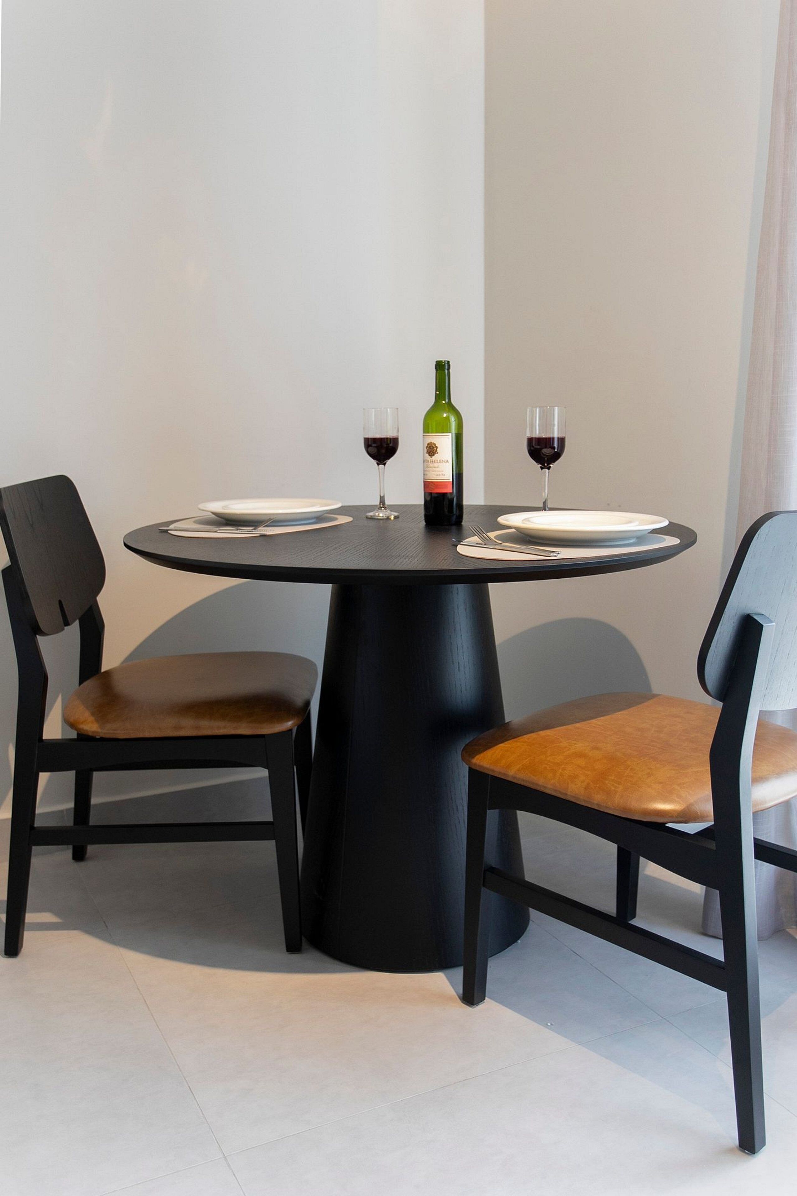 Une table de salle à manger ronde, accompagnée de deux chaises, d’une bouteille de vin et de deux verres à vin.