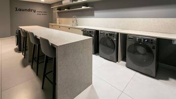 A modern laundry room with a long counter, bar stools, and two front-loading washing machines.