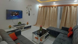 Un salon moderne avec un téléviseur à écran plat fixé au mur, une table basse et des canapés gris agrémentés de coussins orange.