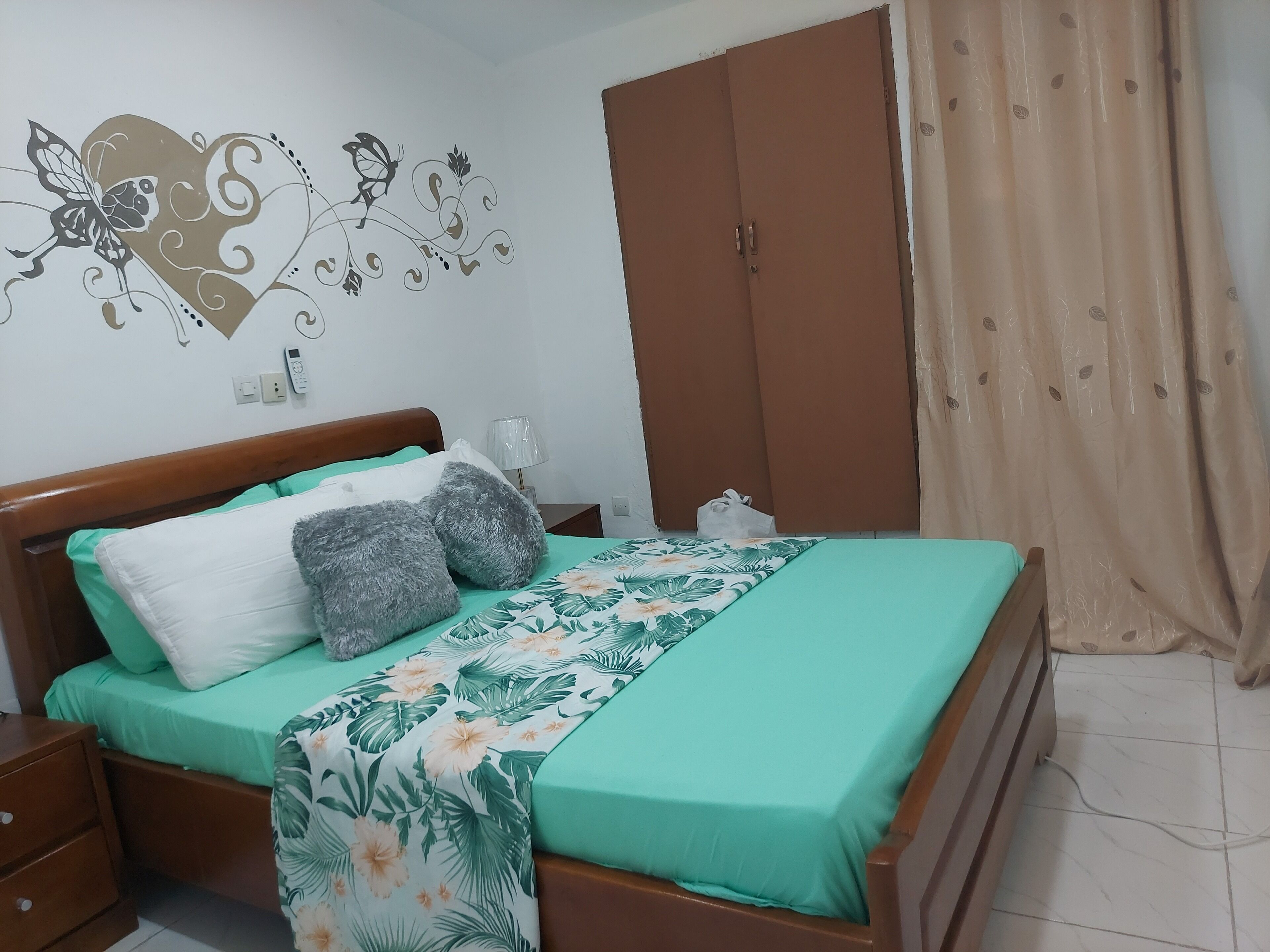 A neatly made bed with a floral bedspread, a wooden headboard, and a wall decoration of a butterfly and heart.