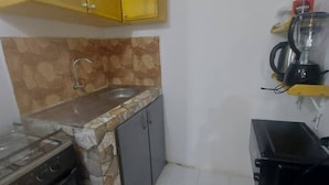 Une cuisine compacte avec un revêtement mural en pierre, une cuisinière à gaz, un évier et un petit réfrigérateur.