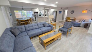 A modern living room with a sectional sofa, a wooden coffee table, and a patterned armchair. A dining area with a round table and chairs is visible in the background. - Spacious 3BR Retreat • King Beds • Close to Siesta Key (Sarasota)