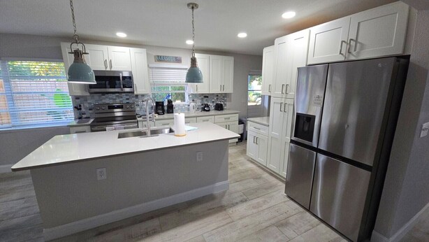 A modern kitchen with white cabinetry, stainless steel appliances, and a central island. - Spacious 3BR Retreat • King Beds • Close to Siesta Key (Sarasota)