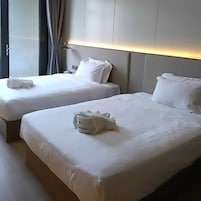 Duas camas de hotel lado a lado, com lençóis e almofadas brancas, uma mesa de cabeceira e um abajur.