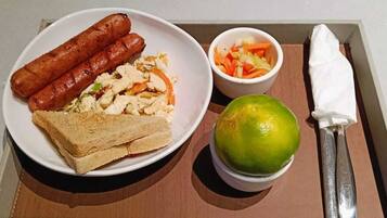 Una bandeja con dos salchichas, huevos revueltos, tostadas, una ensalada pequeña y un limón.