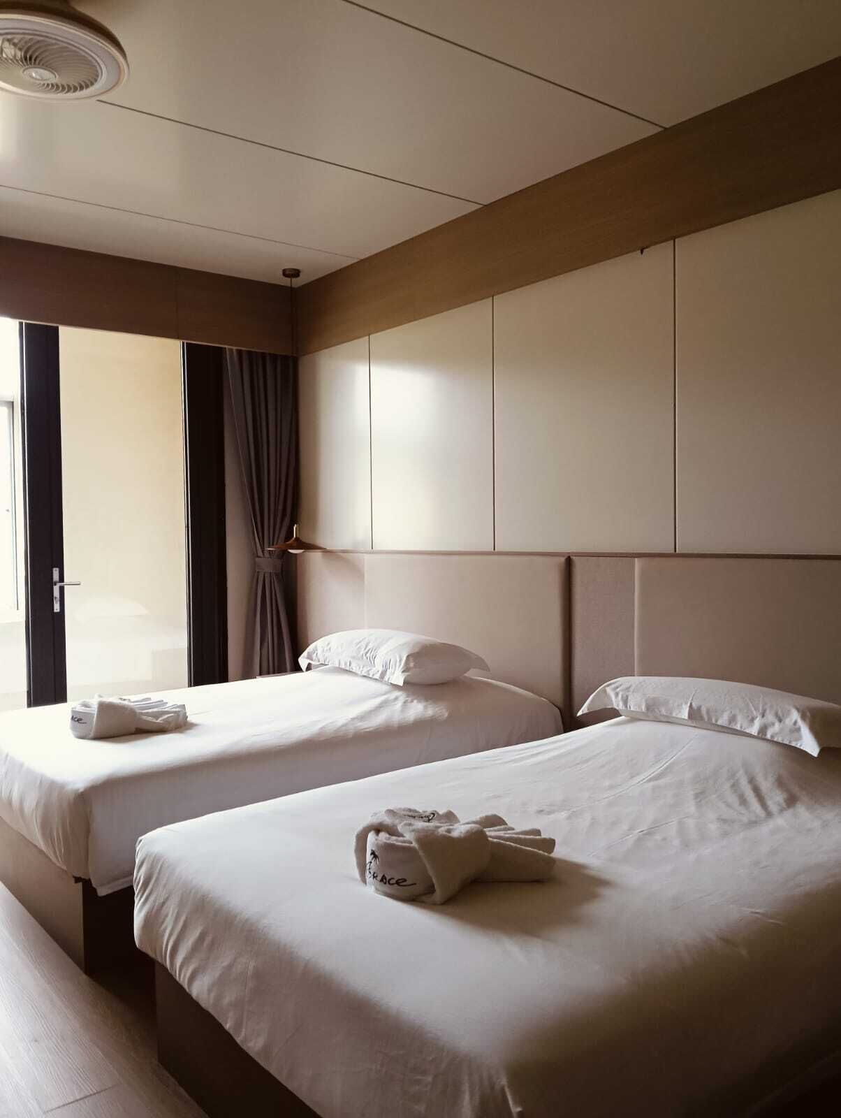 A hotel room with two beds, a ceiling fan, and a large window with curtains.
