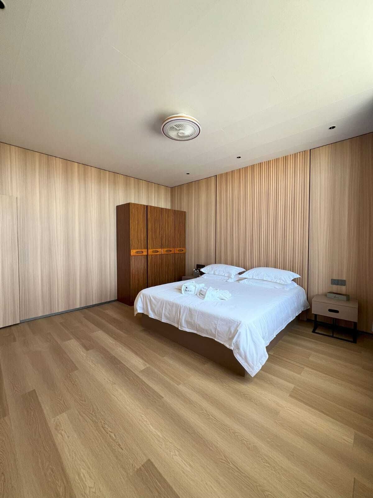 A modern bedroom with a wooden wardrobe, a bed with white linens, and a nightstand.