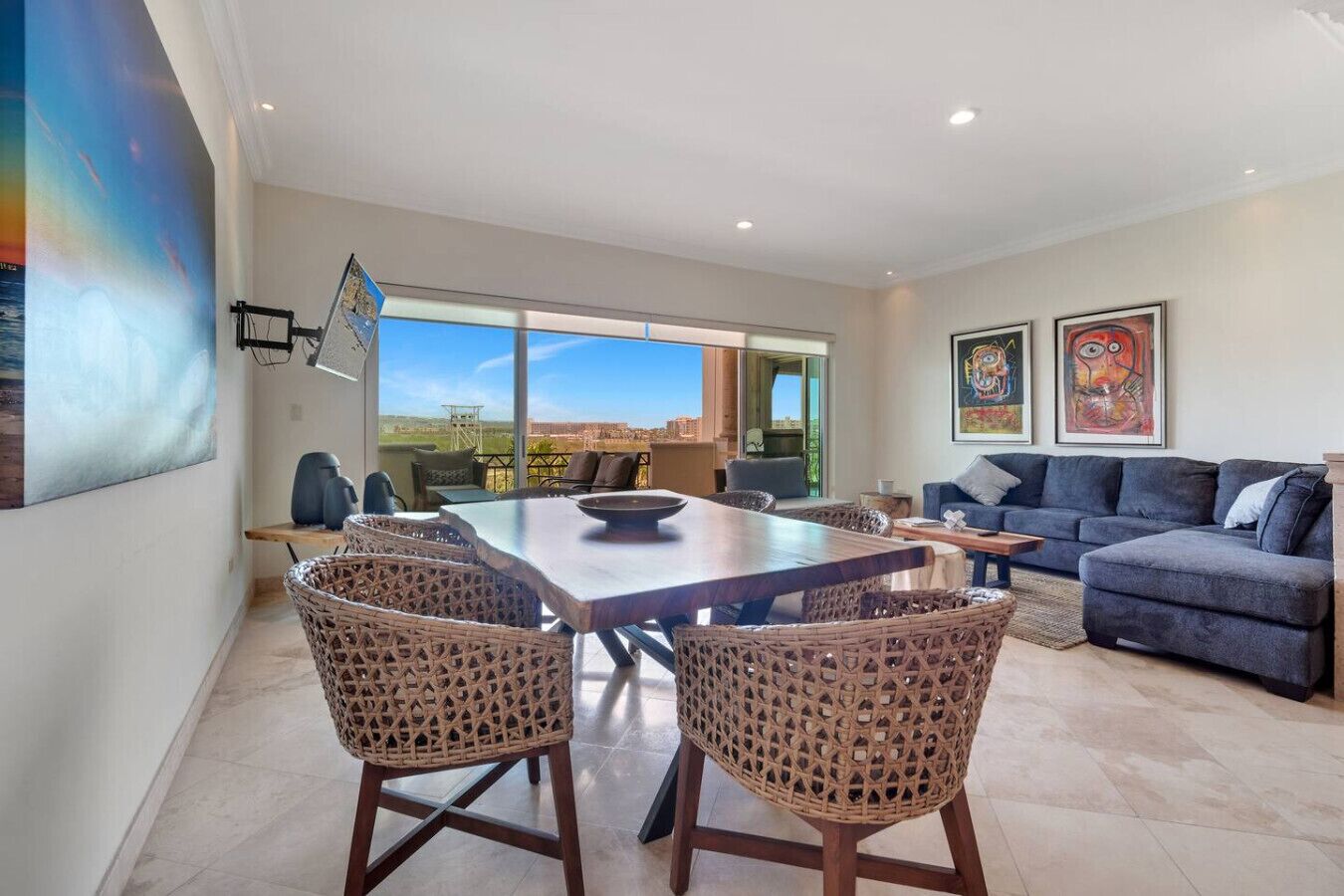 A spacious living area with a dining table, wicker chairs, a sofa, and a balcony with a view.
