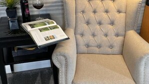 Un sillón con textura, una revista y una botella de vino sobre una mesa negra.