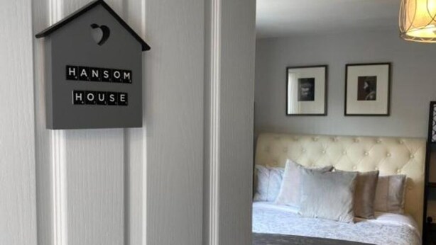 Un dormitorio con cabecera capitonada, una cama con ropa blanca y dos cuadros enmarcados en la pared.