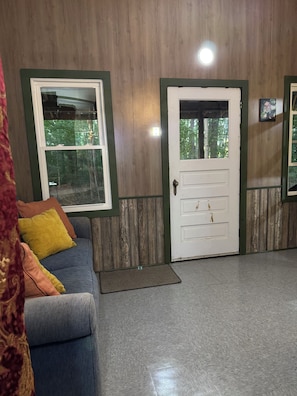 A room with a wooden wall, a white door, a blue sofa with cushions, and a window. - The Mill Creek Hideout (Mill Creek)