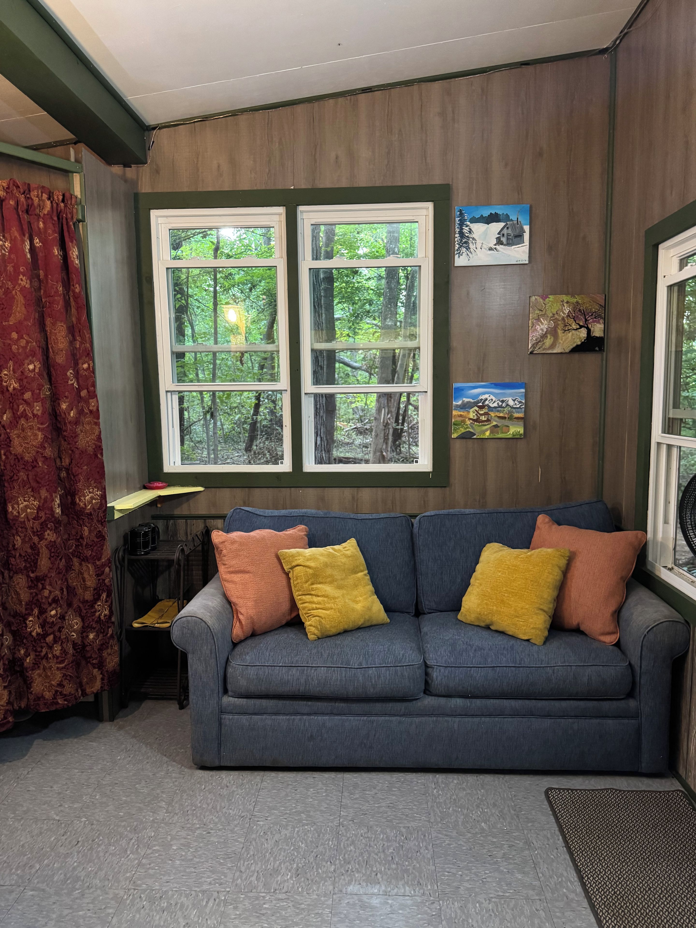 A room with a grey sofa, red curtains, and a window with a view of trees.