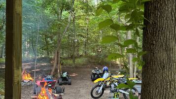 A forested area with dirt paths and ATVs parked near a fire pit.