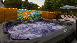 A hot tub with a colorful mural in the background, surrounded by wooden fences and string lights.