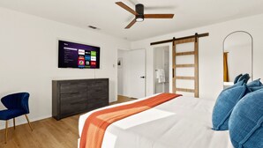 A modern bedroom with a bed, a TV mounted on the wall, a wardrobe, a chair, and a ceiling fan.