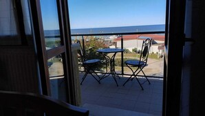 A balcony with two chairs and a table, overlooking a coastal area with buildings and a clear sky.