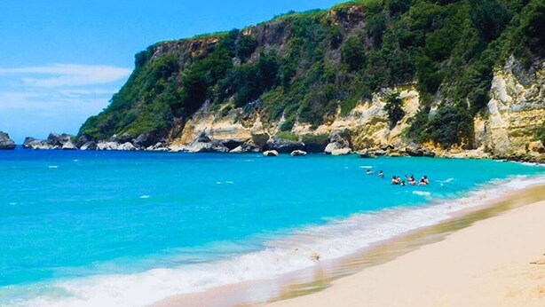 A beach with clear turquoise water, rocky cliffs, and a sandy shore. - Beachside Near Airport Near Golf Course (Aguadilla)