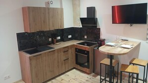 A compact kitchen with wooden cabinets, a black countertop, a built-in oven, a microwave, and a small dining area with a table and two stools. - la chambre des plaisirs secrets Manduel (Manduel)