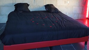 A bed with a black bedspread and red frame, a white brick wall, and a red light fixture above. - la chambre des plaisirs secrets Manduel (Manduel)
