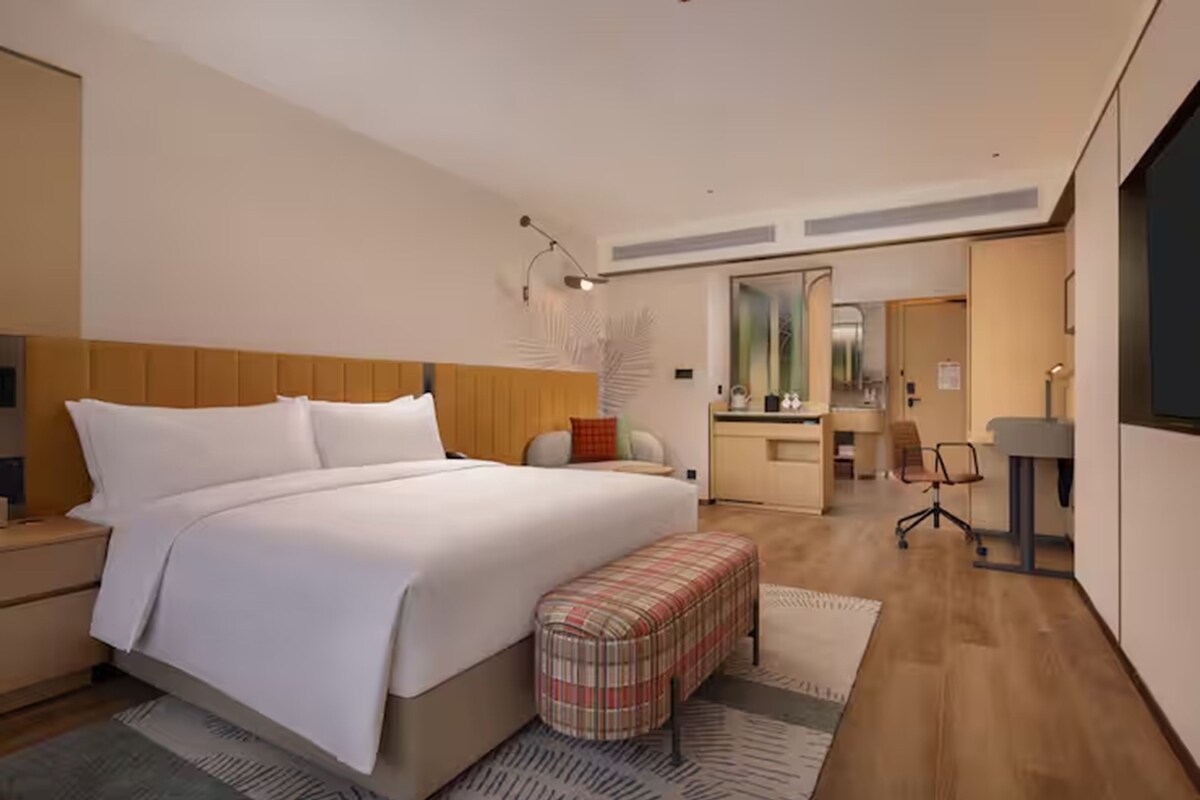 Una habitación de hotel moderna con una cama grande, un pequeño banco, un escritorio y un espejo.