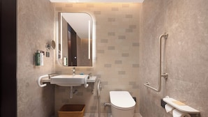 Un baño moderno con lavamanos, espejo, inodoro y barras de apoyo.
