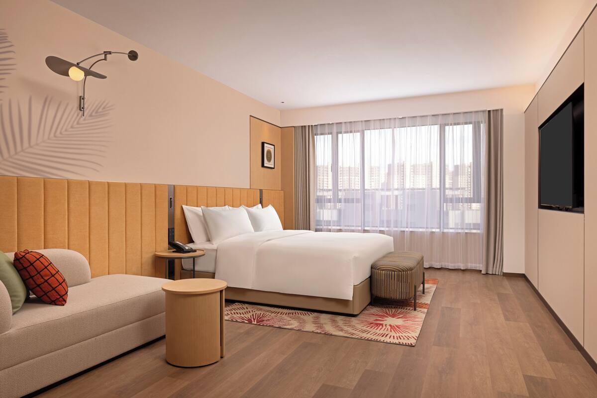Una habitación de hotel moderna con cama, sofá, una mesita y televisor.