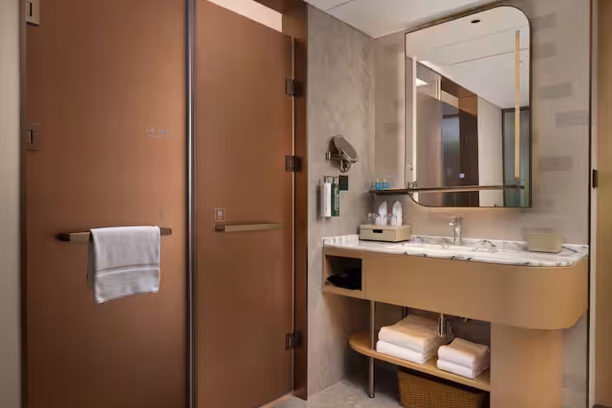 Un baño moderno con mampara de vidrio, lavamanos de mármol y un espejo grande.