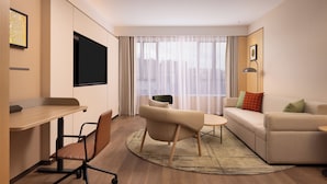 Una habitación de hotel moderna con televisión de pantalla plana, sofá, mesita de centro y zona de comedor.