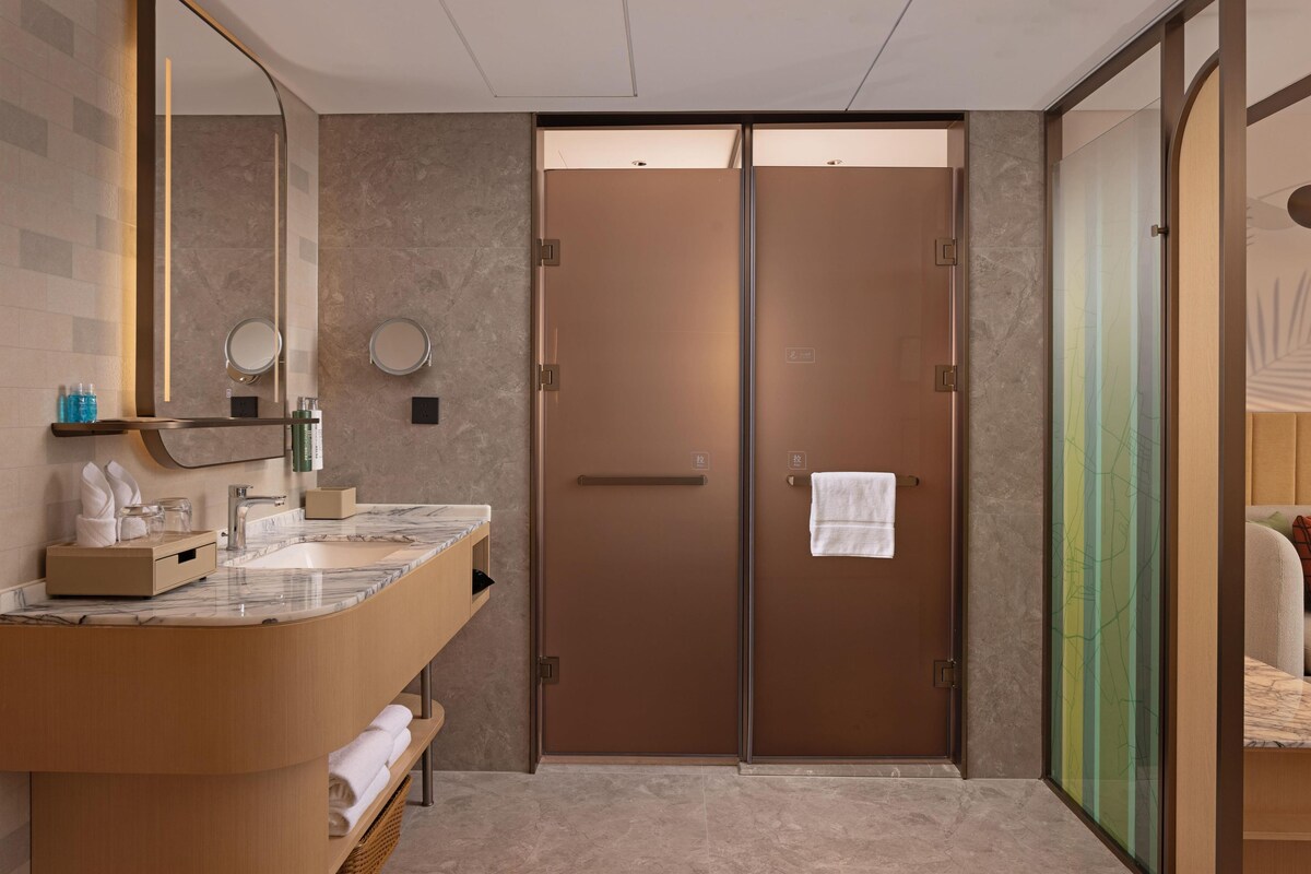 Un baño moderno con un lavamanos de mármol, un espejo grande y una puerta de vidrio que da a un dormitorio.