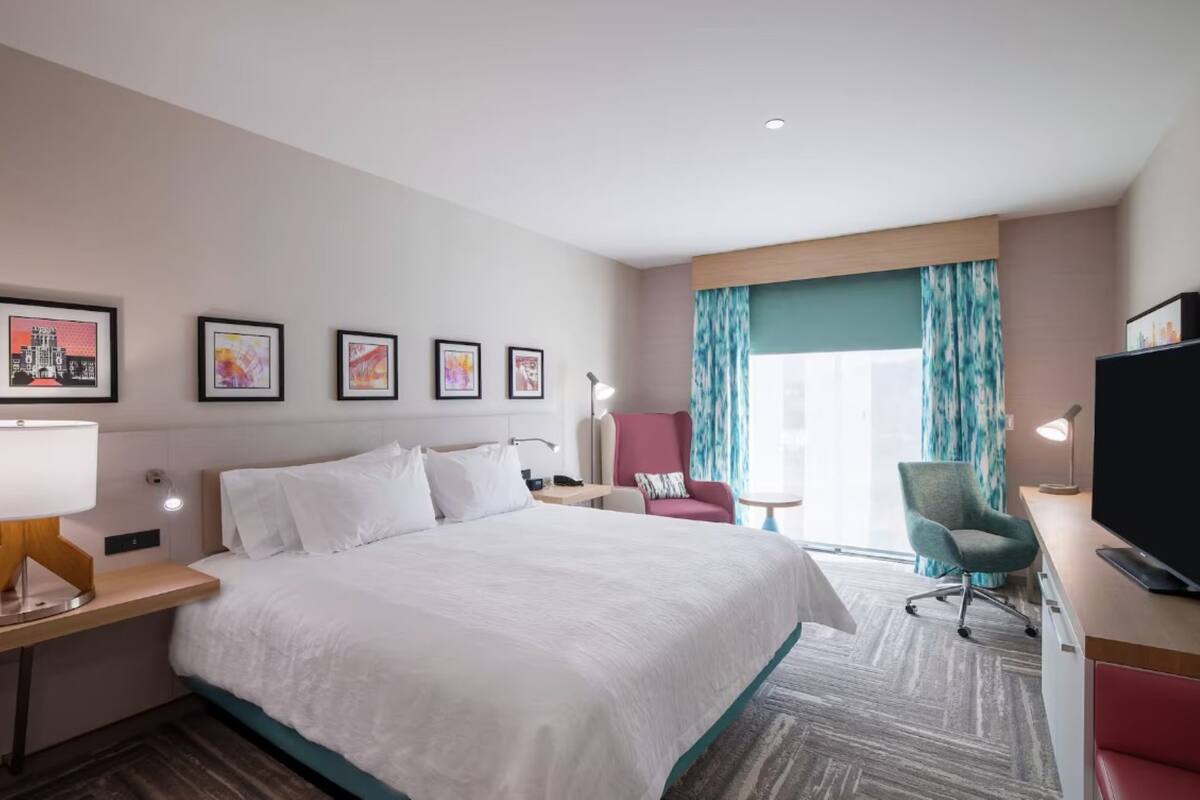 Habitación de hotel con una cama grande, un escritorio con computadora, televisión y cuadros en la pared.