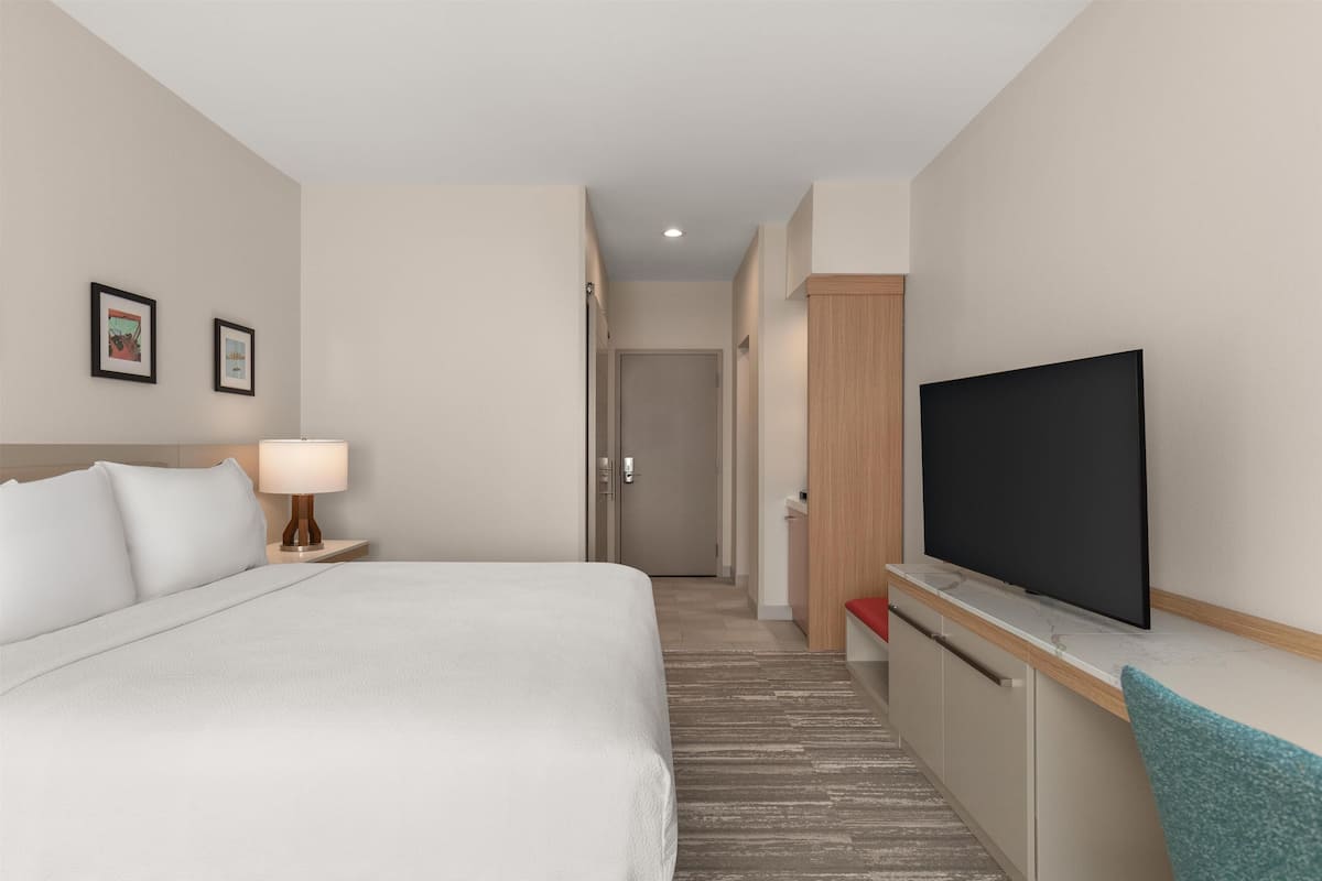 Una habitación de hotel con cama, televisor, escritorio y puerta que da a otra habitación.
