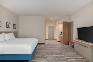 A hotel room with a bed, a flat-screen TV, a desk with a computer, and a door leading to a bathroom.