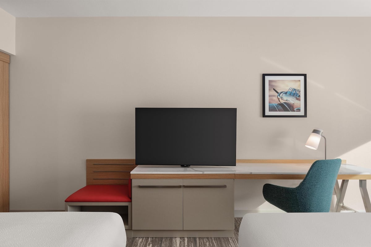 Una habitación de hotel moderna con una televisión de pantalla plana, un escritorio, una silla, una mesita de noche y un cuadro enmarcado en la pared.