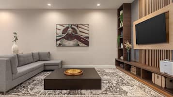A modern living room with a sectional sofa, a coffee table, a large flat-screen TV, and a decorative wall piece.
