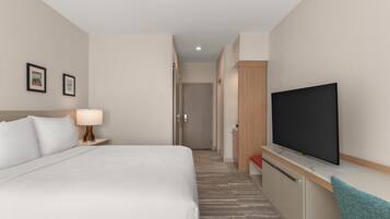 Una habitación de hotel con cama, televisión, escritorio y puerta que da a un pasillo.