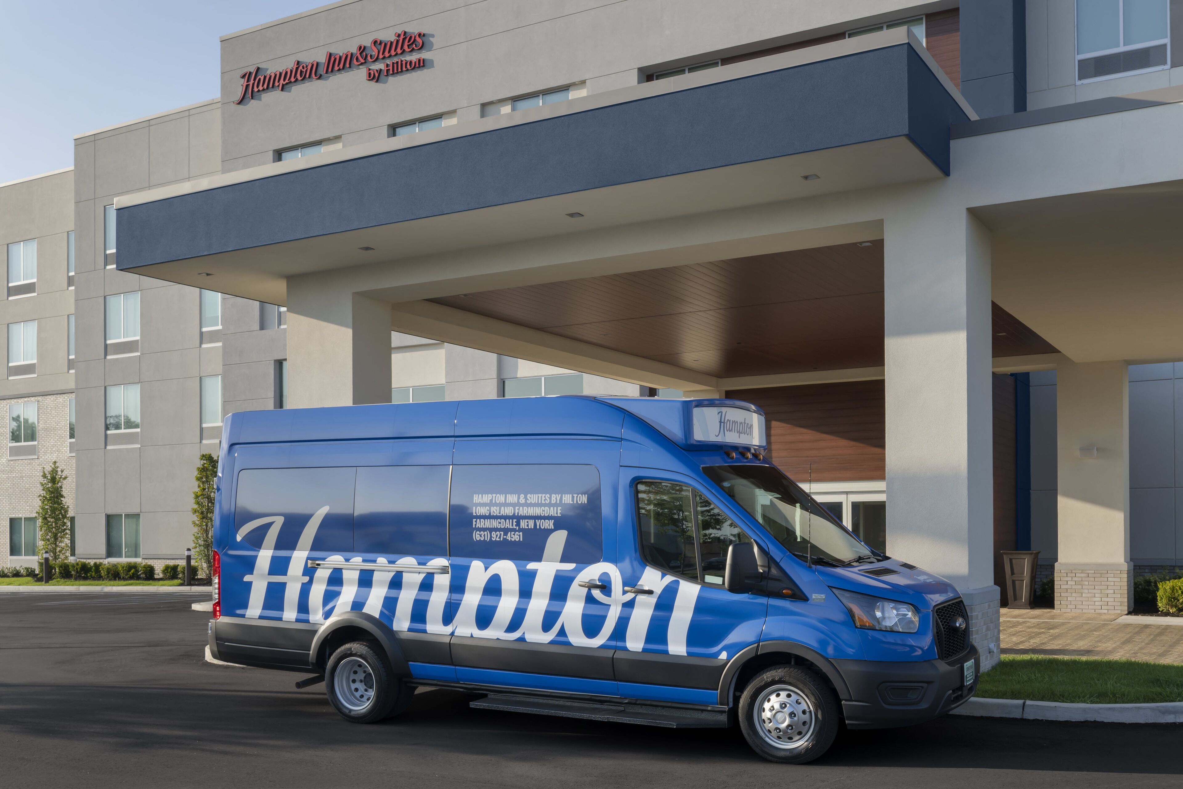 A blue Hampton Inn & Suites van parked in front of the hotel.