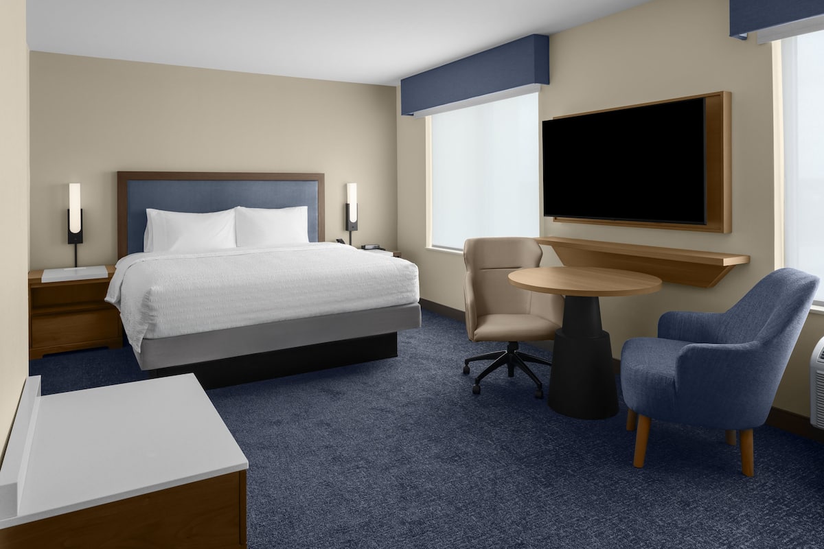 Una habitación de hotel con una cama, mesitas de noche, un escritorio, una silla, una mesa redonda, un televisor y una ventana.
