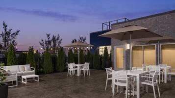 An outdoor patio area with a white table and chairs, two umbrellas, and a modern building in the background.