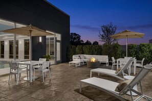 Eine Terrasse im Freien mit weißer Möbel, darunter Liegestühle und ein Esstisch, sowie einem Feuerkorb.