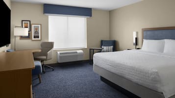 A hotel room with a bed, a desk, a chair, a window, and a wall-mounted TV.